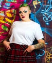 Punk girl with attitude. Green hair, tattoos, facial piercings. Graffiti background.