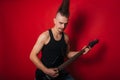 A Punk man with a black electric guitar with a mustache and a large mohawk. Photo rock musician in the studio on a red background Royalty Free Stock Photo