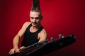 A Punk man with a black electric guitar with a mustache and a large mohawk. Photo rock musician in the studio on a red background Royalty Free Stock Photo