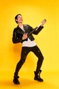 Punk, young guy with baseball bat like playing guitar and smiling over yellow background. Concept of music, subculture