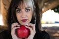 Punky girl with blonde and brunette hair holds a red apple in her hands and stares at it. The girl is a witch from the fairy tale Royalty Free Stock Photo