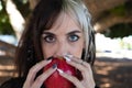 Punky girl with blonde and brunette hair holds a red apple in her hands and stares at it. The girl is a witch from the fairy tale Royalty Free Stock Photo