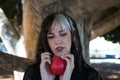 Punky girl with blonde and brunette hair holds a red apple in her hands and stares at it. The girl is a witch from the fairy tale Royalty Free Stock Photo