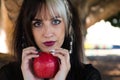 Punky girl with blonde and brunette hair holds a red apple in her hands and stares at it. The girl is a witch from the fairy tale Royalty Free Stock Photo