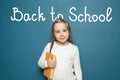 Pupil with braids holding yellow book on blue background. Back to school and childhood concept Royalty Free Stock Photo