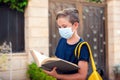 Pupil with face mask holding book outdoor. Back to school Royalty Free Stock Photo