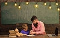 Pupil with teacher at school. Tutor helping kid to write letters in copybook. Man and boy sit at desk with laptop and