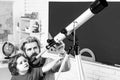 Pupil watching stars with a teacher. Astronomy telescope. Happy cute industrious child is sitting at a desk indoors