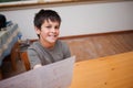 Boy child presenting worksheet at desk in study area with side table holding books, copy space Royalty Free Stock Photo