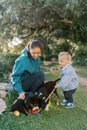 Puppies sniffing a wheeled toy on a stick from a little girl next to her squatting mom