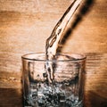 Pure fresh water is pouring into glass on wooden background close up, healthy drink Royalty Free Stock Photo