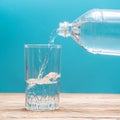 Pure healthy cool water is pouring into a glass from a plastic bottle on a blue background Royalty Free Stock Photo