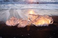 Pure Ice Shining on Black Volcanic Sand at Sunset. Icebergs from Glacier in Sun Rays. Clear Ice in Ocean Waves. Famous Royalty Free Stock Photo