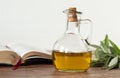 Pure olive oil in a glass jar, an open Bible Book, and a green olive branch on a wooden table with white background