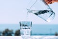 Pure water from a jug is poured into a glass beaker. Glass with water on the background of the sea Royalty Free Stock Photo