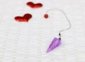 Amethyst crystal quartz pendulum and two red hearts on white cloth.Valentine`s concept