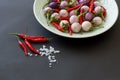 Purple asian eggplants and hot red peppers on a green plate and nearby with salt crystals on a black background. Side view