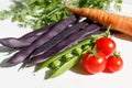 purple beans in pods, green peas in a pod, red cherry tomatoes, greens and raw carrots Royalty Free Stock Photo