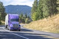 Purple big rig semi truck with reefer semi trailer running with load on the winding mountain road Royalty Free Stock Photo