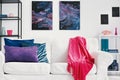 Purple, blue and green pillows and pink blanket on white sofa in stylish living room with galaxy graphic on the wall Royalty Free Stock Photo