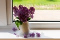 A purple bouquet of lilacs in a white jug stands on the windowsill of a country house