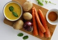 Purple bowl of potato and carrot cream soup with ingredients on wooden cutting board Royalty Free Stock Photo