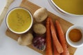 Purple bowl of potato and carrot cream soup with ingredients on wooden cutting board Royalty Free Stock Photo
