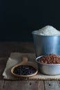 Purple-brown rice in a wooden ladle, jasmine red rice in a zinc cup, jasmine rice in a zinc bucket placed on sackcloth on a rustic Royalty Free Stock Photo