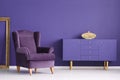 Purple cabinet with a golden vase, comfy armchair and frame in a Royalty Free Stock Photo