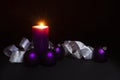 Purple Christmas balls with burning candle and white ribbon on black background Royalty Free Stock Photo