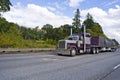 Purple classic big rig semi truck transporting covered commercial cargo on flat bed semi trailer Royalty Free Stock Photo
