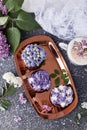 Purple cupcakes, aesthetics desserts on golden tray, coffee cup with melted marshmallow among lilac flowers background