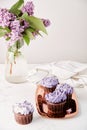 Purple cupcakes on the golden tray and bouquet of lilac flowers. Vertical photo