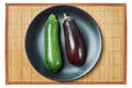 Purple eggplant and pale green zucchini squash on a gray plate on a cane tablecloth