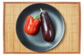 Purple eggplant and red bell pepper on a gray plate on a cane tablecloth