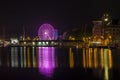 Purple Ferris wheel reflected in the water at the harbor.