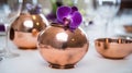 a purple flower is in a copper vase on a white table cloth with wine glasses and wine glasses behind it, and a wine glass in the Royalty Free Stock Photo