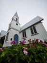 Purple flowers blooming in front of white historic wooden building St Peter Anglican church in Akaroa New Zealand