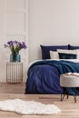 Purple flowers in blue glass vase on stylish bedside table next to king size bed Royalty Free Stock Photo