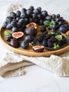 Purple fruits, berries and green mint leaves. Blackberries, grapes, plums and figs in a wooden tray on a white marble background. Royalty Free Stock Photo