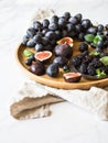 Purple fruits, berries and green mint leaves. Blackberries, grapes, plums and figs in a wooden tray on a white marble background. Royalty Free Stock Photo