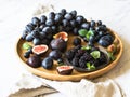 Purple fruits, berries and green mint leaves. Blackberries, grapes, plums and figs in a wooden tray on a white marble background. Royalty Free Stock Photo