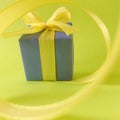 Purple gift box at the end of the spiral yellow ribbon, green background, square.