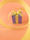 Purple Gift box at the end of the spiral yellow ribbon, orange background, vertical. Royalty Free Stock Photo