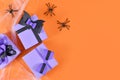 Purple Halloween paper gift boxes with bows, spiders and cobweb on side of orange background with copy space