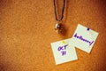 Purple handwriting on white paper note, pin on cork board with yellow and purple pin, metal skull pendant necklace as background