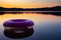 Purple inflatable swimming ring on top of still lake water surface at sunset. Rubber rescue wheel and colourful evening sky and Royalty Free Stock Photo