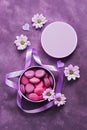 Purple macaroons in a gift box on a beautiful purple background decorated with flowers. View from above