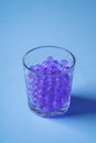 Purple marbles in drinking transparent glass blue background angle view Royalty Free Stock Photo