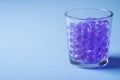 Purple marbles in drinking transparent glass blue background angle view Royalty Free Stock Photo